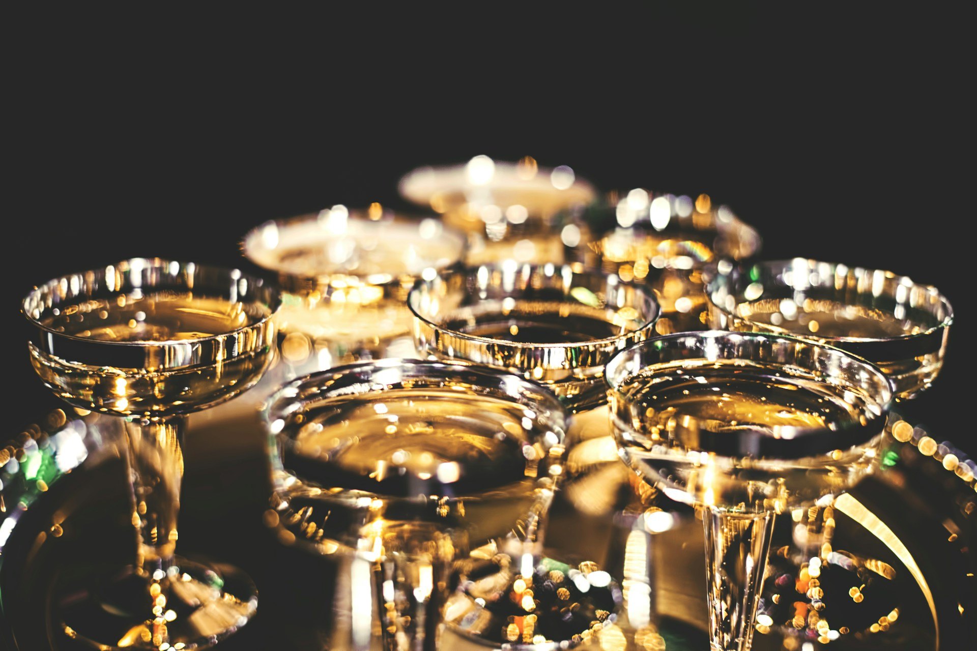 Des coupes de champagne dorées serrées sur un plateau, dans la pénombre d'une réception