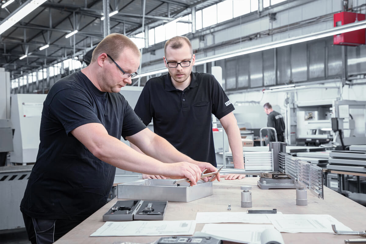 Two technicians measuring a housing at a workbench in a production hall in Germany