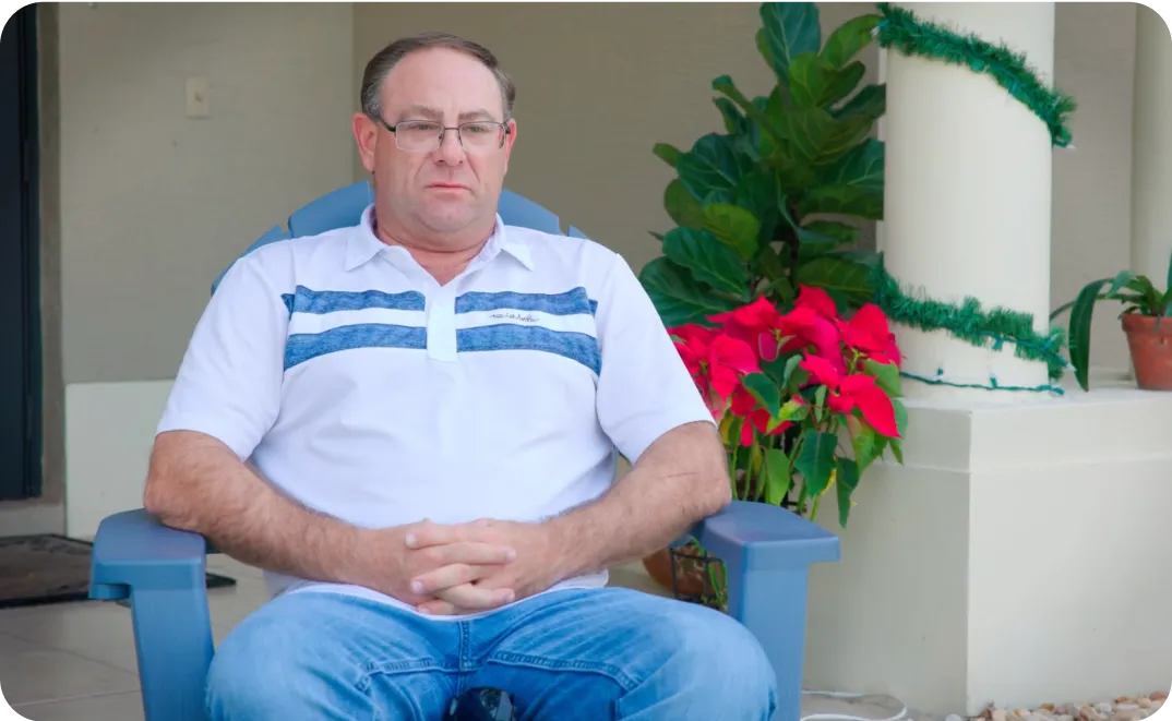 A man sitting in a blue chair in front of a potted plant.