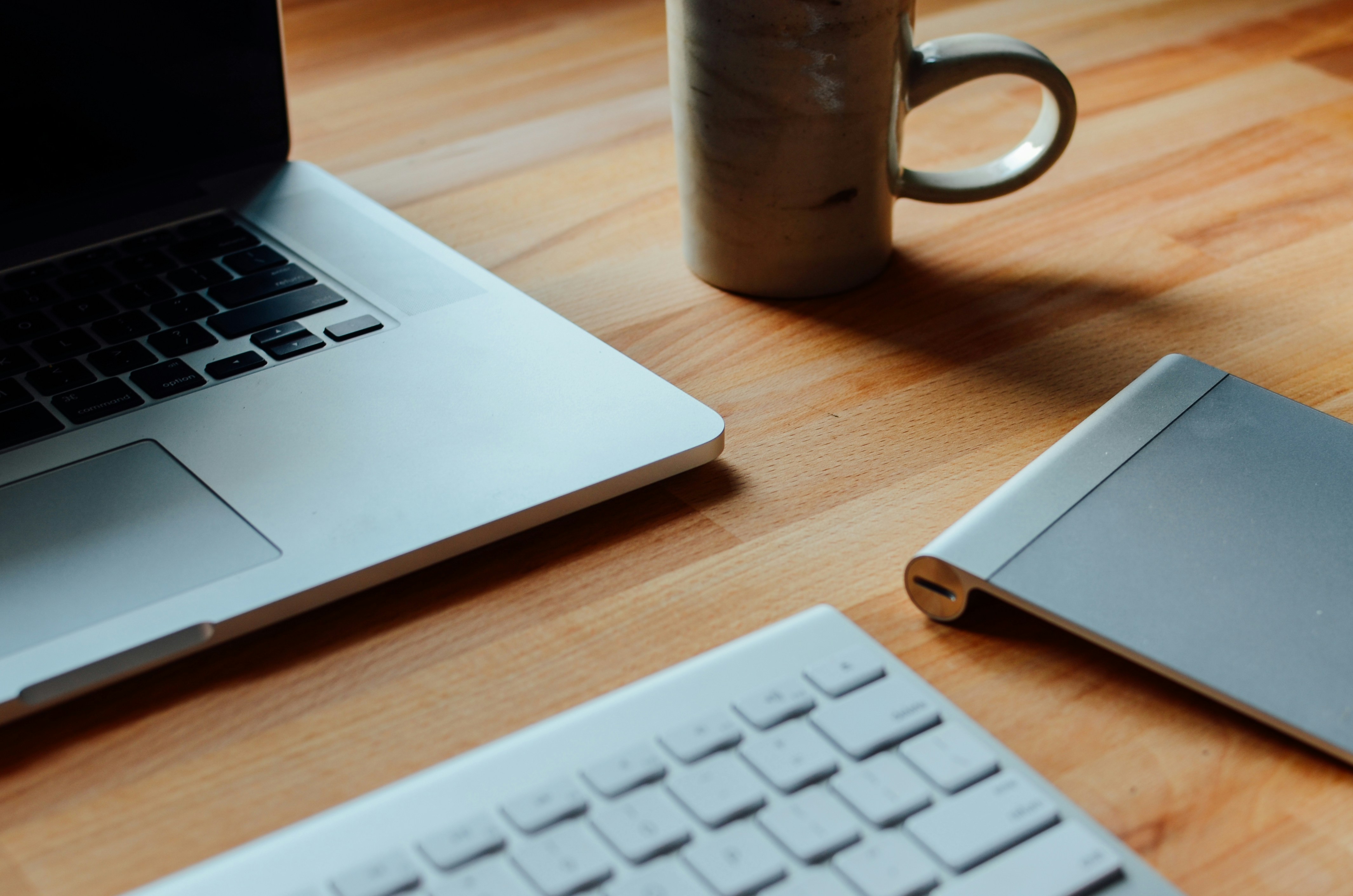 Laptop, klawiatura, trackpad i kubek na drewnianym biurku