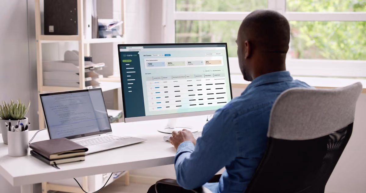 Man sitting at a desk working on a computer with dual monitors showing a dashboard and code.