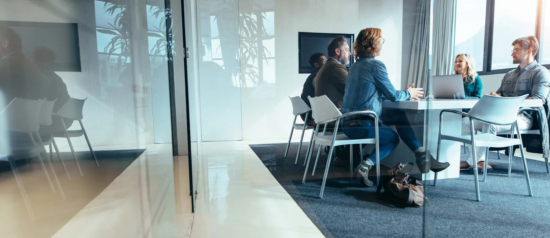 Five people sitting around a white table in a bright office conference room with large windows.