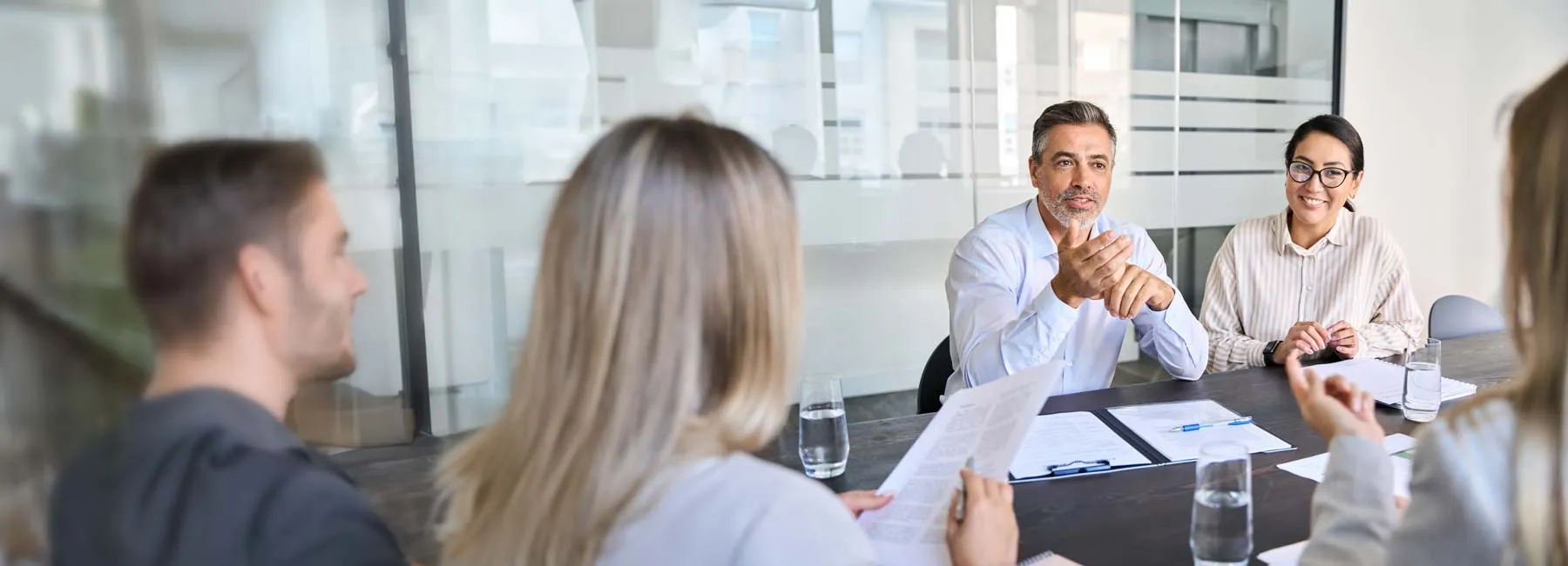 Four people sit at a table in a meeting room, discussing papers and smiling.