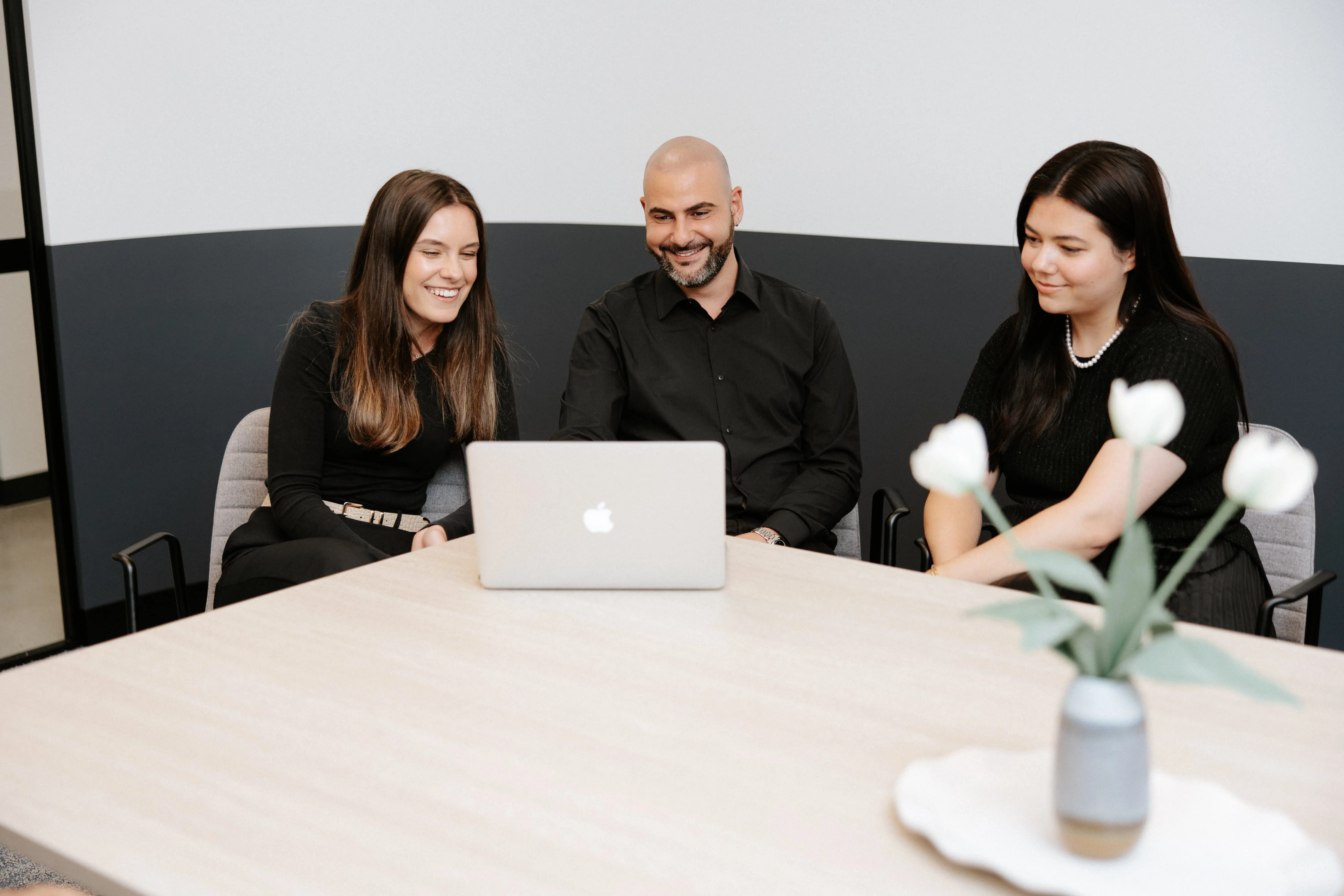 Three people sitting at a table with a laptop.