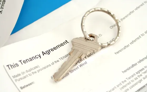  Close-up of a house key on a keyring placed over a tenancy agreement document.