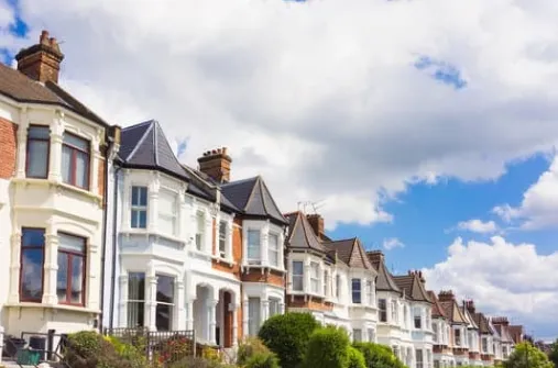 A row of traditional terraced houses with brick and white facades under a partly cloudy blue sky.