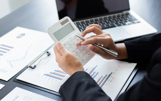 Close-up of a person calculating financial data with a calculator and pen, alongside financial charts and a laptop—ideal for illustrating mortgage planning or property investment analysis.