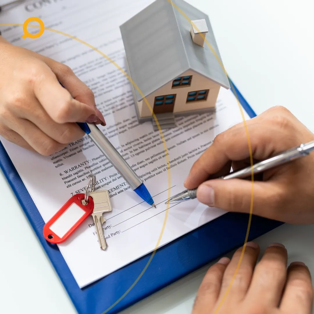 A close-up shot shows two people's hands, one holding a blue pen and the other a silver pen, signing a document on a blue clipboard. A small model house and a set of keys with a red tag are placed on the document.