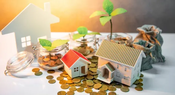 Small house models with coins, money jars, and growing plants symbolising real estate investment and wealth building.