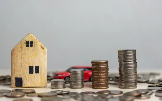 Stacked coins with a wooden house model and red car representing property investment, savings, and financial growth.