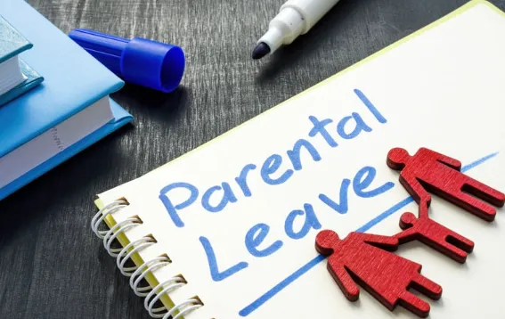 Notebook with text 'Parental Leave' beside wooden figures of parents and child, symbolizing family support and employee benefits. 