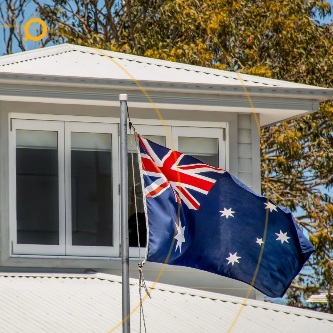 Australian flag flying outside a modern home with white cladding and a gable roof, symbolising homeownership in Australia.