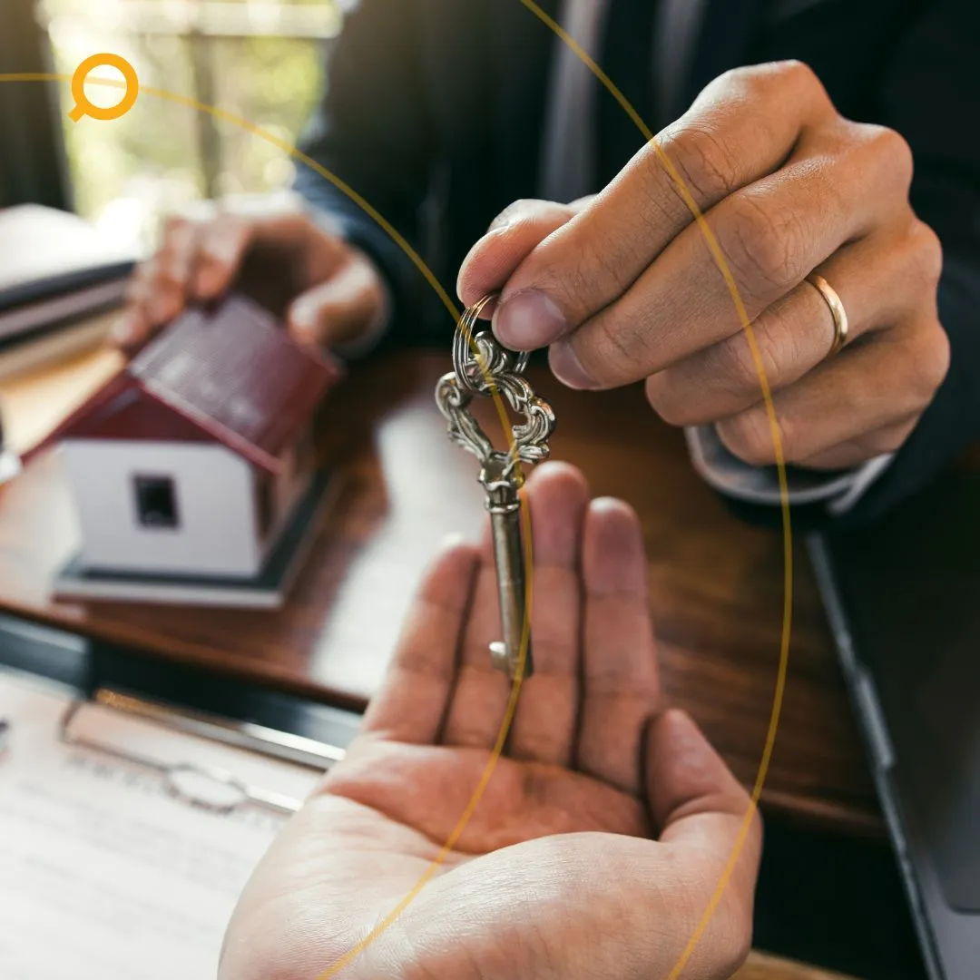Close-up of a buyers' agent handing over ornate house keys to a buyer, with a miniature home model and contract paperwork in the background symbolising property ownership.
