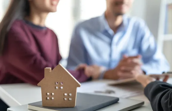 Smiling couple meeting with a property consultant, with a small house model on the table symbolising homeownership or property investment.