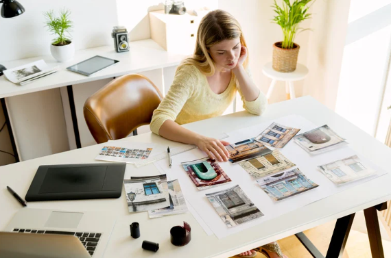 Young woman sitting at a desk reviewing printed property photos and architectural designs, planning a real estate or renovation project.