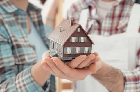  Close-up of a couple holding a miniature model house together, symbolizing home ownership, real estate investment, or buying a new home.