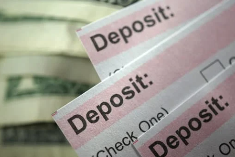 Stack of deposit slips with blurred dollar bills in the background, representing bank deposits or financial transactions.