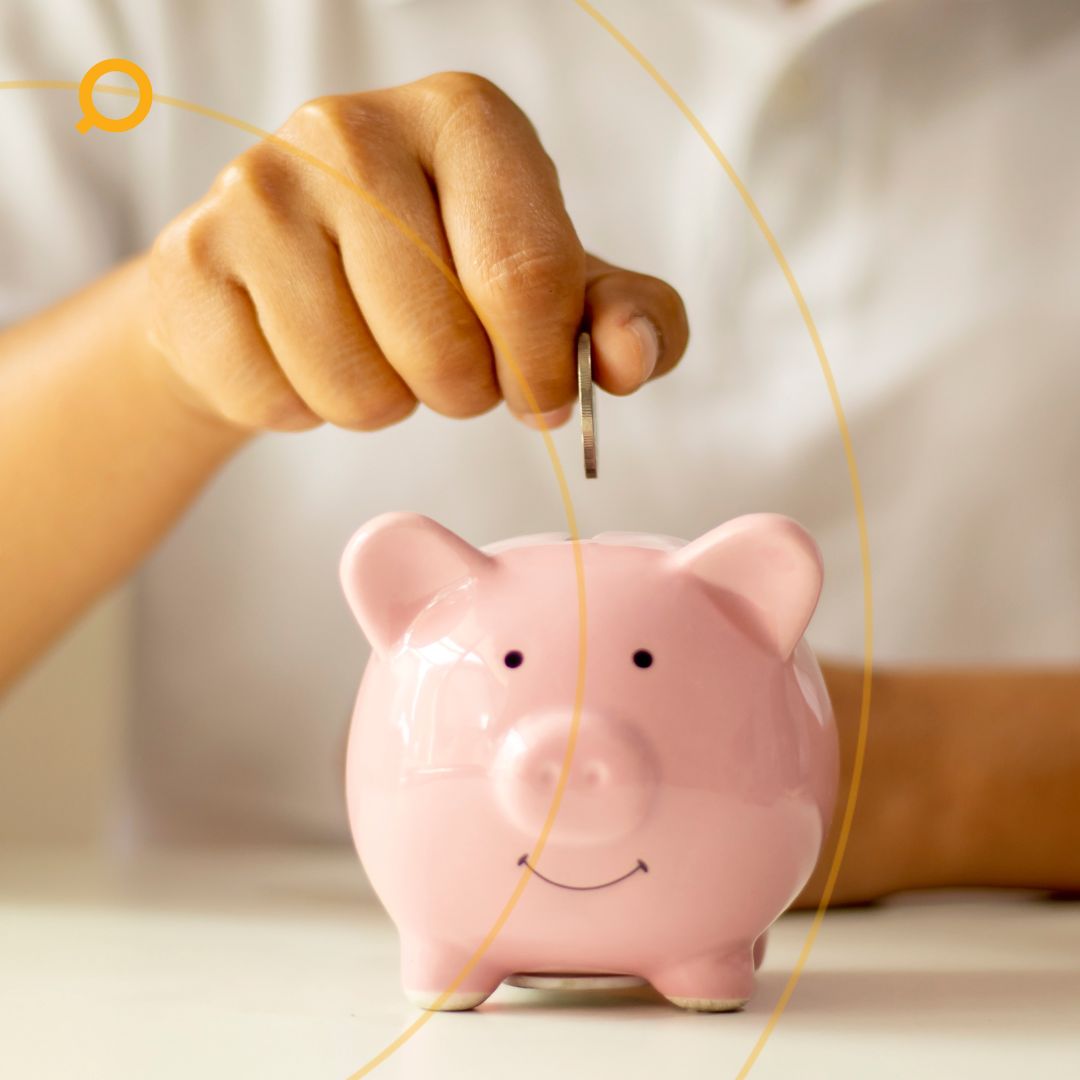 Hand placing a coin into a pink piggy bank on a white table, symbolising personal savings, budgeting, and financial responsibility.