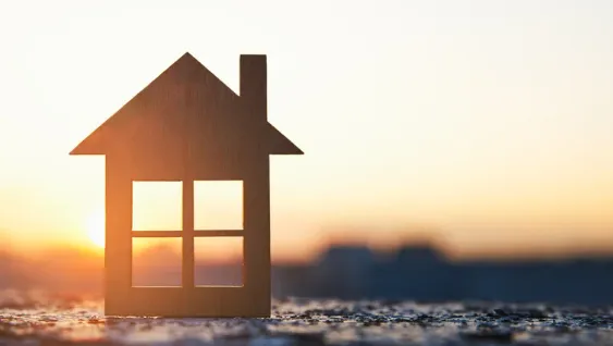 Wooden house model silhouette against a warm sunrise background, symbolising new beginnings and real estate opportunities.