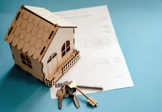 Small wooden house model and keys placed on a contract document, representing property purchase or lease agreement.