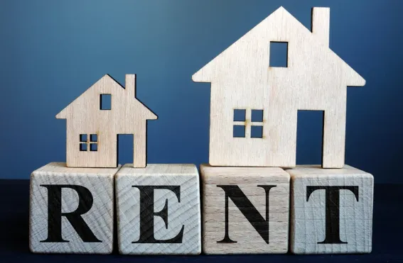 Wooden house models on letter blocks spelling RENT, symbolising rental property market and real estate investment