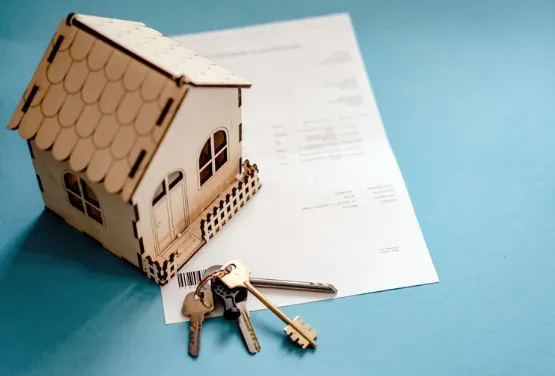 Wooden model house and metal keys placed on top of a property contract, symbolising real estate purchase or mortgage agreement.