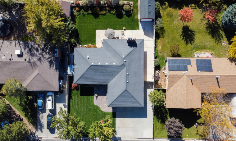 Aerial view of suburban house with landscaped backyard, driveway, and solar panels on nearby home.