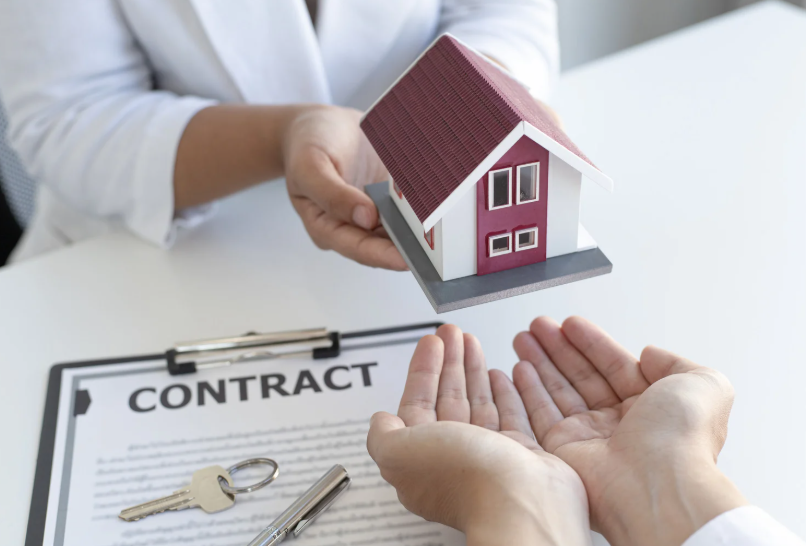 Agent handing keys to a buyer over a property contract and miniature house model.