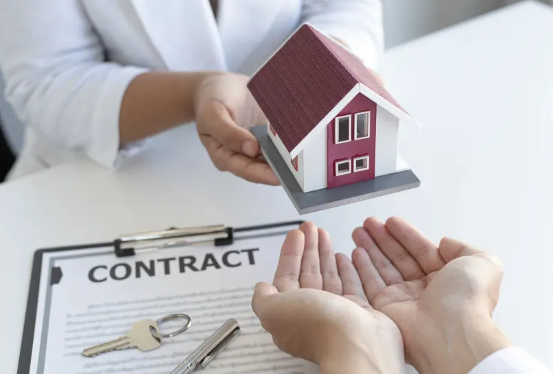 Agent handing keys to a buyer over a property contract and miniature house model.