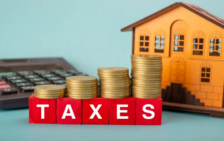 Stacks of coins on red blocks spelling “TAXES” with a calculator and model house, symbolising property tax and real estate investment costs.