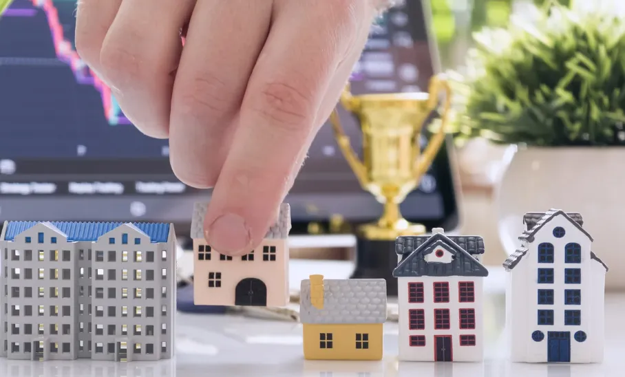 Hand picking miniature house model among different properties, symbolising real estate investment and property selection."