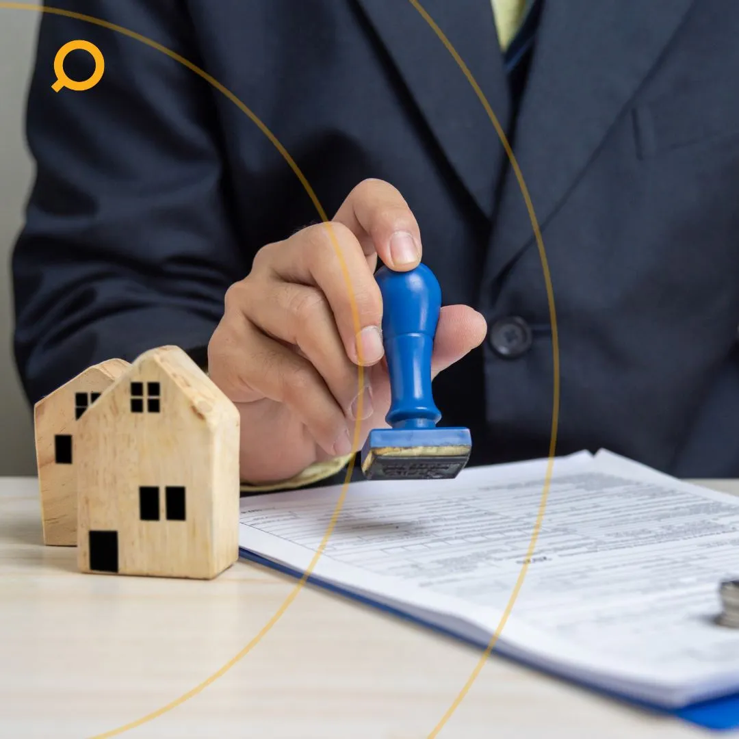 Individual stamping contract with wooden house models and stacks of coins, symbolising property investment and loan approval.