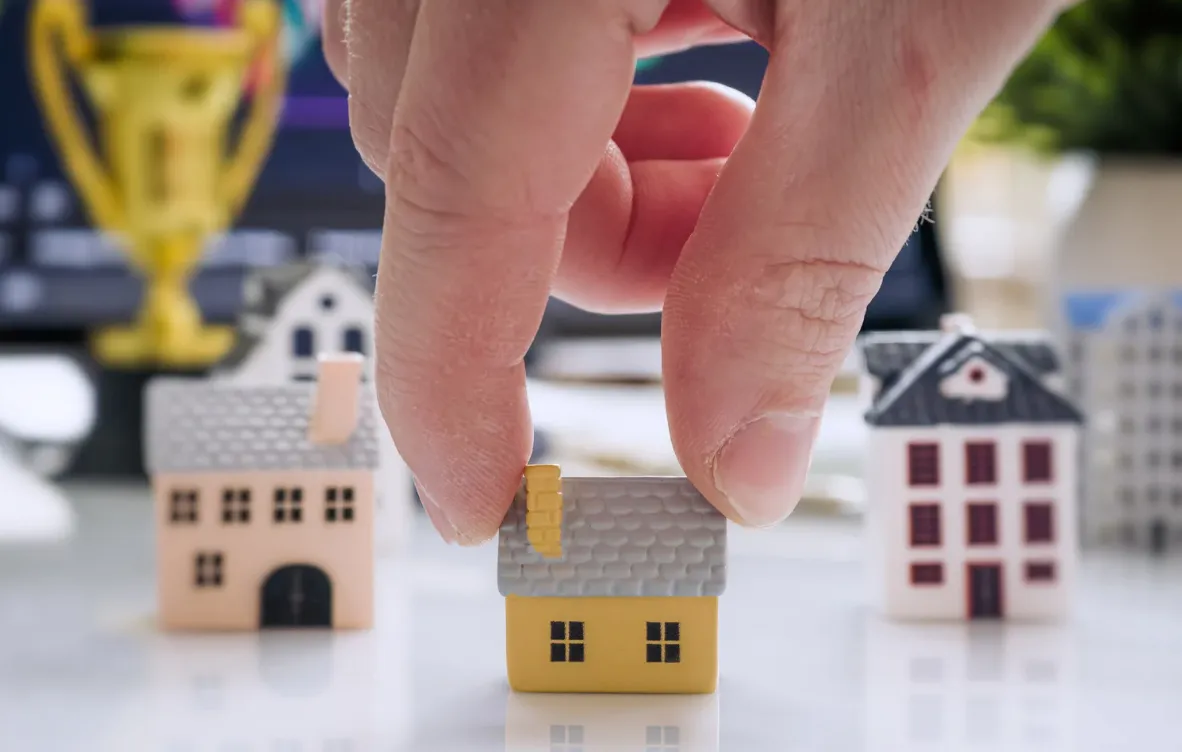 Close-up of a hand placing a miniature house among other small house models, representing property investment and portfolio building.