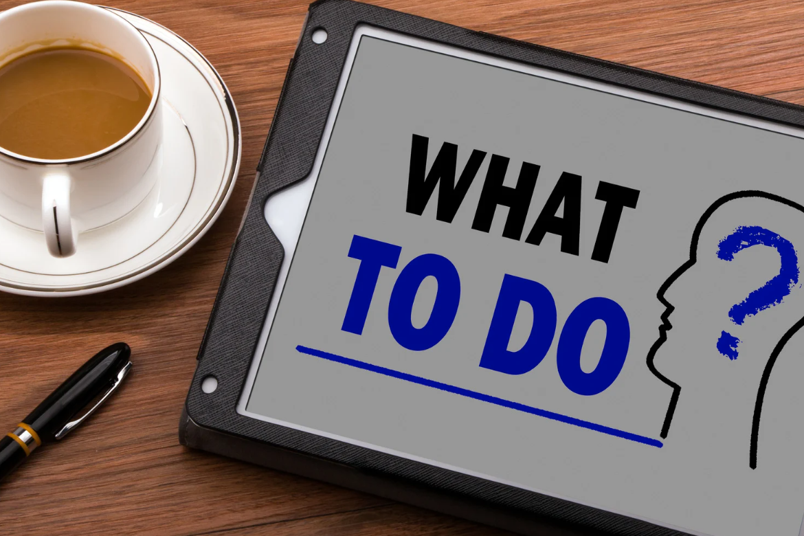 Tablet screen showing the words “What To Do?” beside a coffee cup and pen on a wooden desk, symbolising decision-making in property investment.