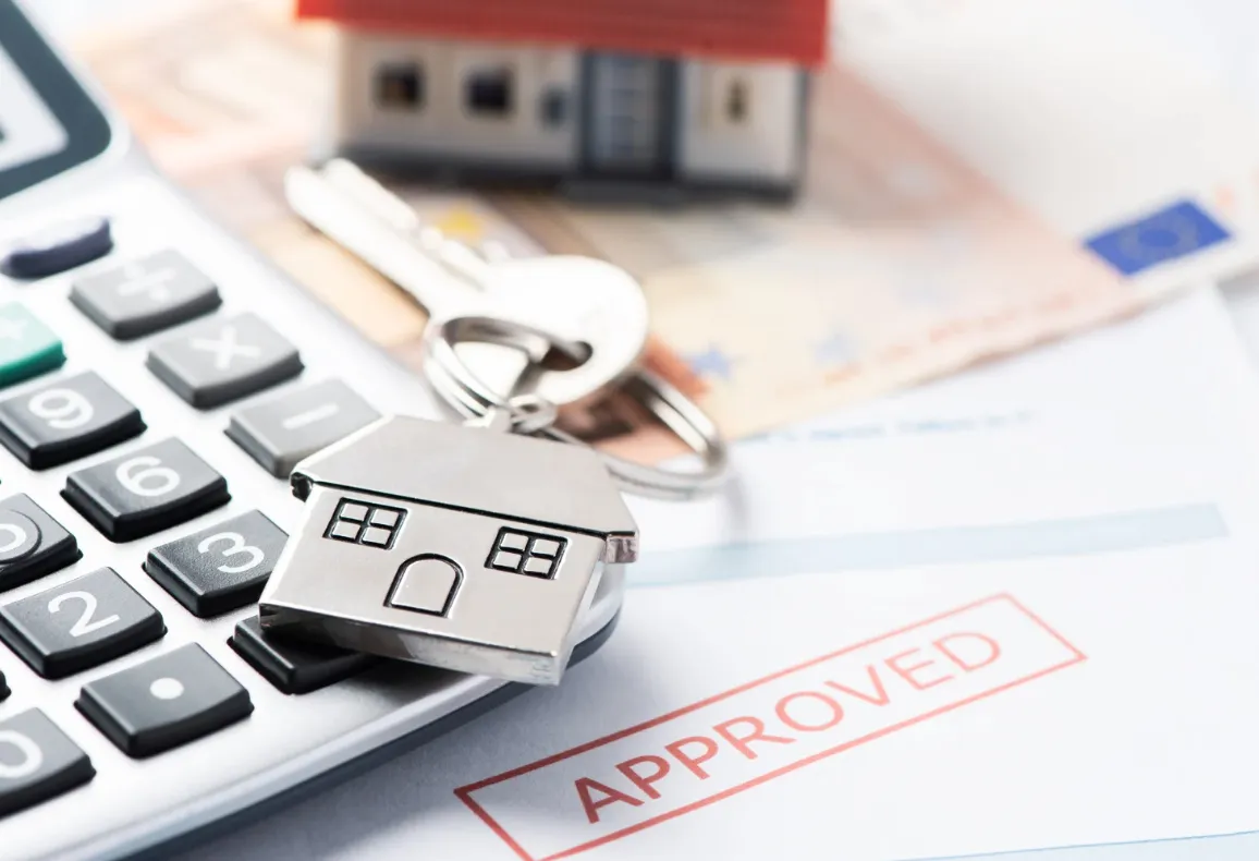House-shaped keychain on calculator with approved finance document, illustrating successful property loan or home loan approval process.