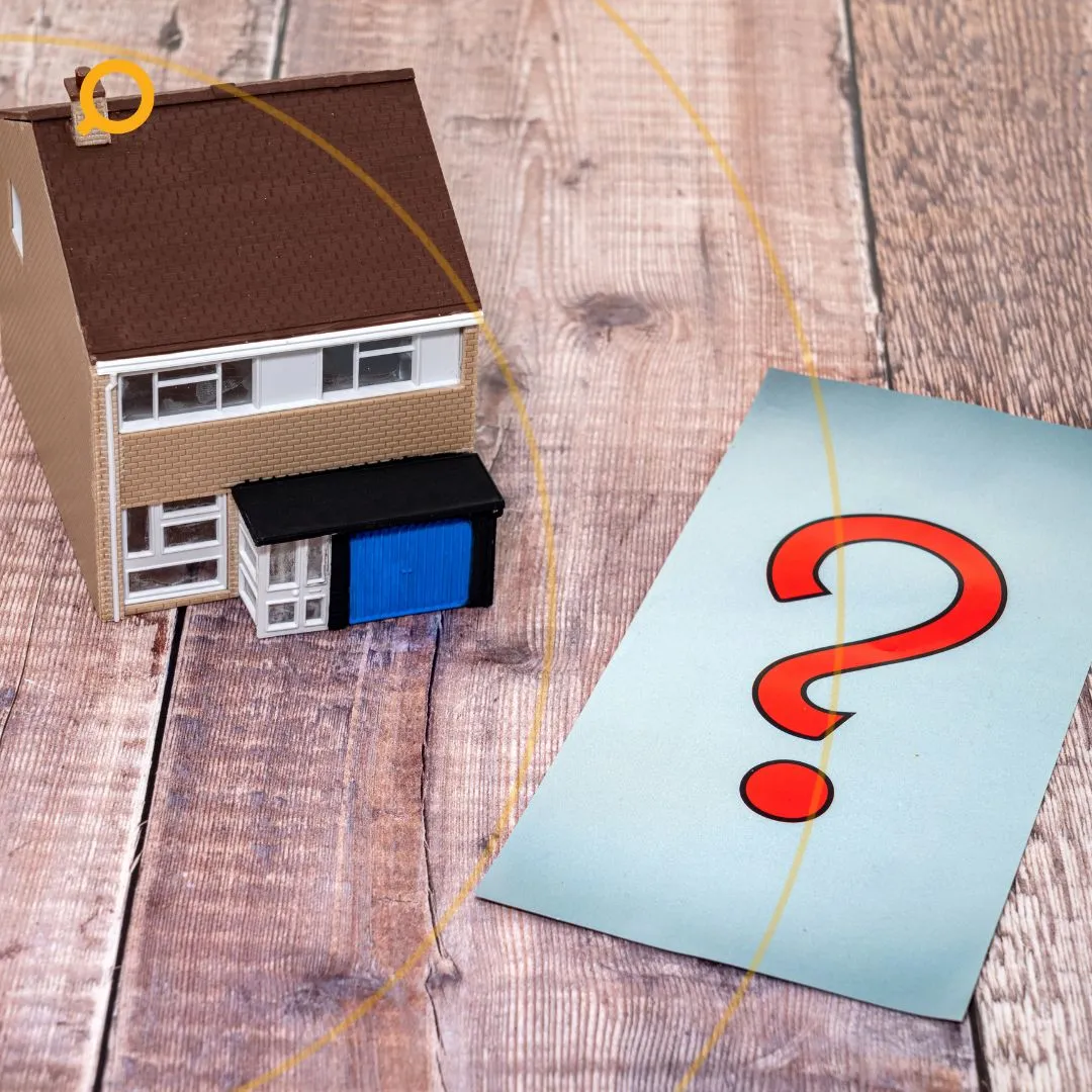 A miniature house placed on a table beside a paper with a "question mark" on it
