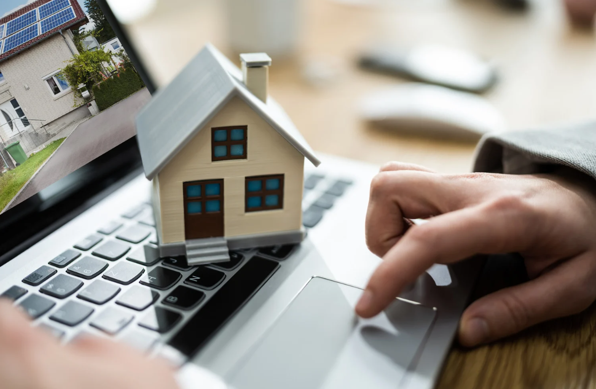 An individual browsing for an investment property to buy with a miniature house placed on his laptop.