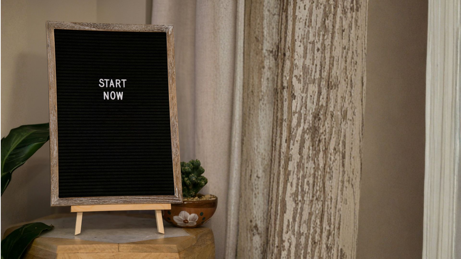 A small desk sign that says "Start Now" in white letters on a black background