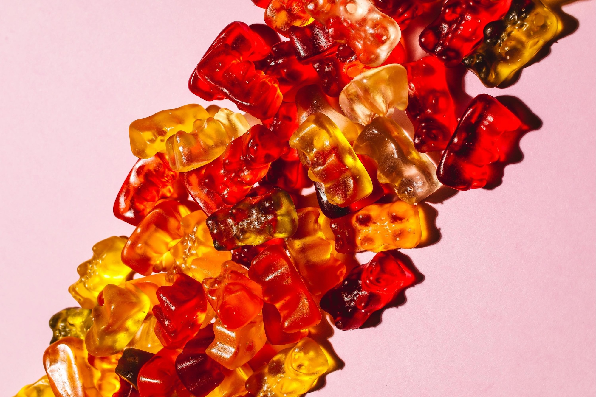A pile of colorful gummy bears on a pink background