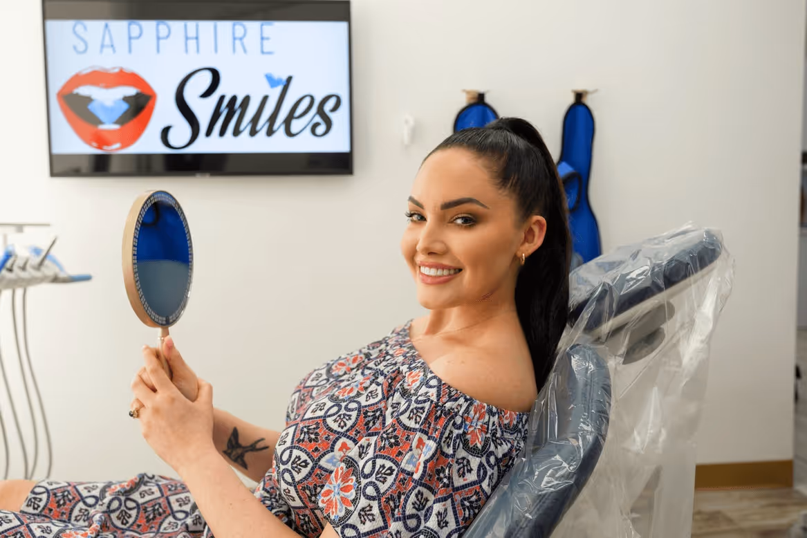 Smiling woman holding a mirror in a modern dental office, showcasing a beautiful smile after cosmetic treatment from the best cosmetic dentist in Houston.