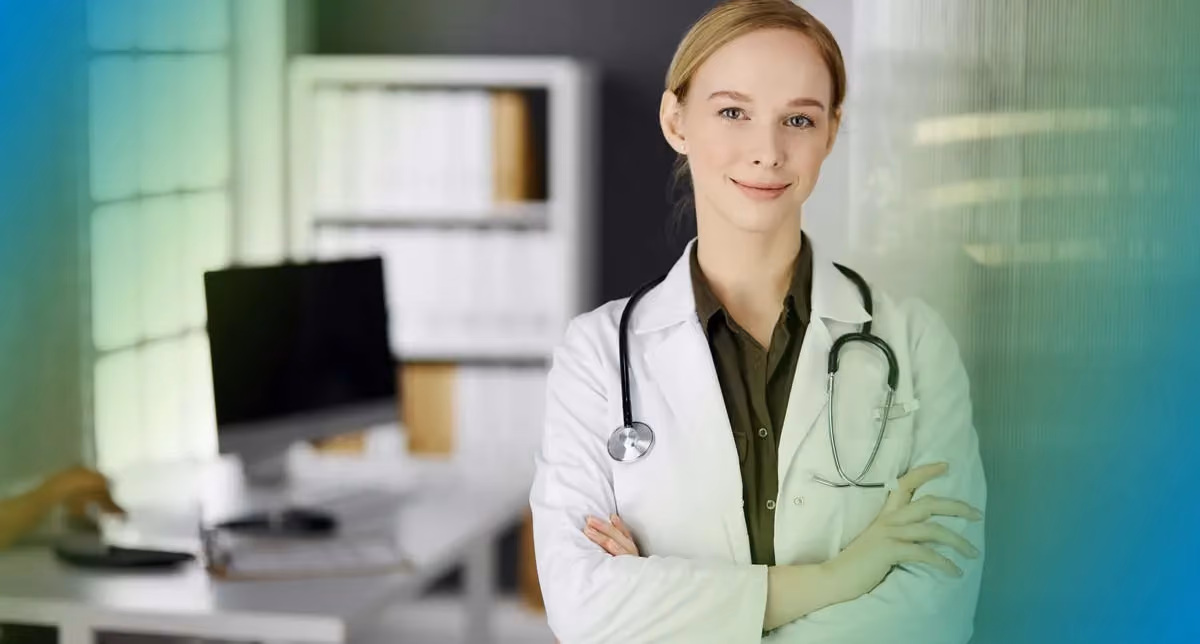 A physician stands in a white coat with a stethoscope around their neck and arms crossed.