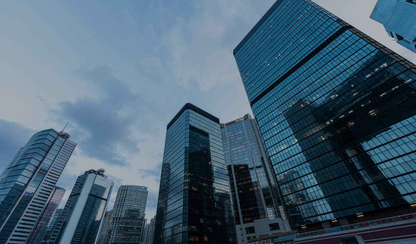 Modern city skyline with glass office buildings viewed from street level under a cloudy sky.