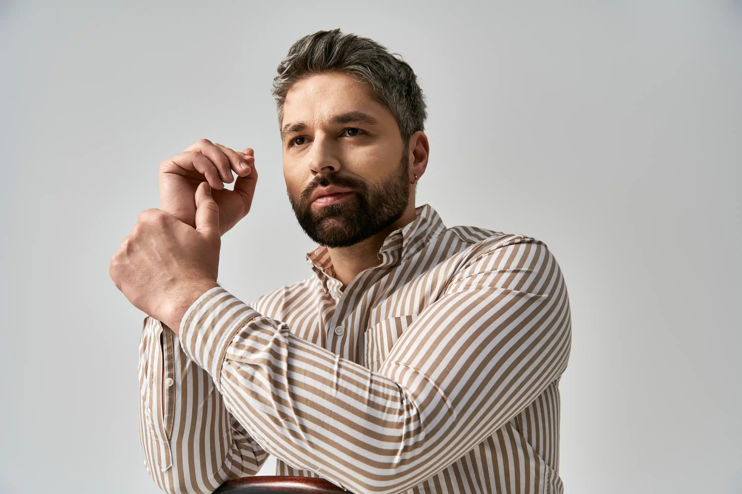 Man with brown and white striped shirt adjusting sleeve against a plain light background.