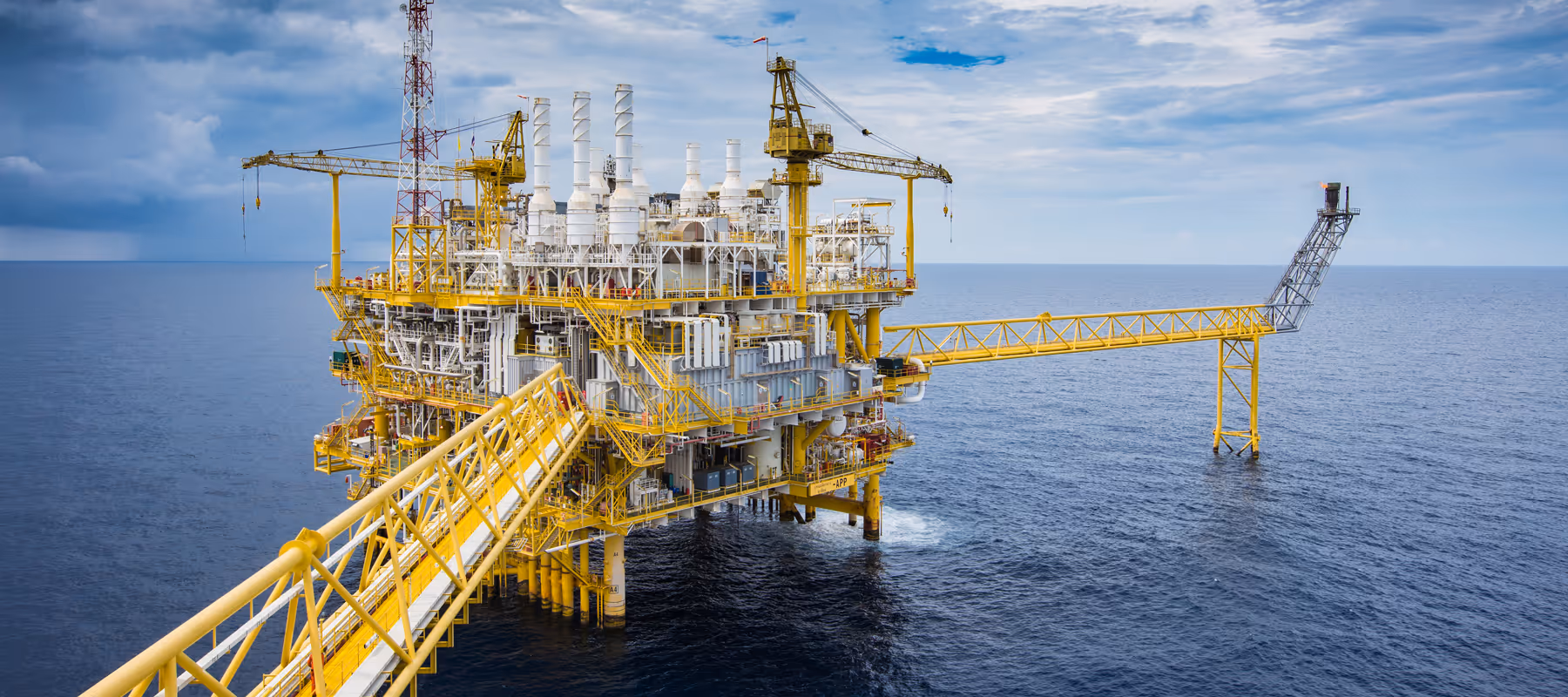 Yellow offshore oil rig platform in calm sea under partly cloudy sky.