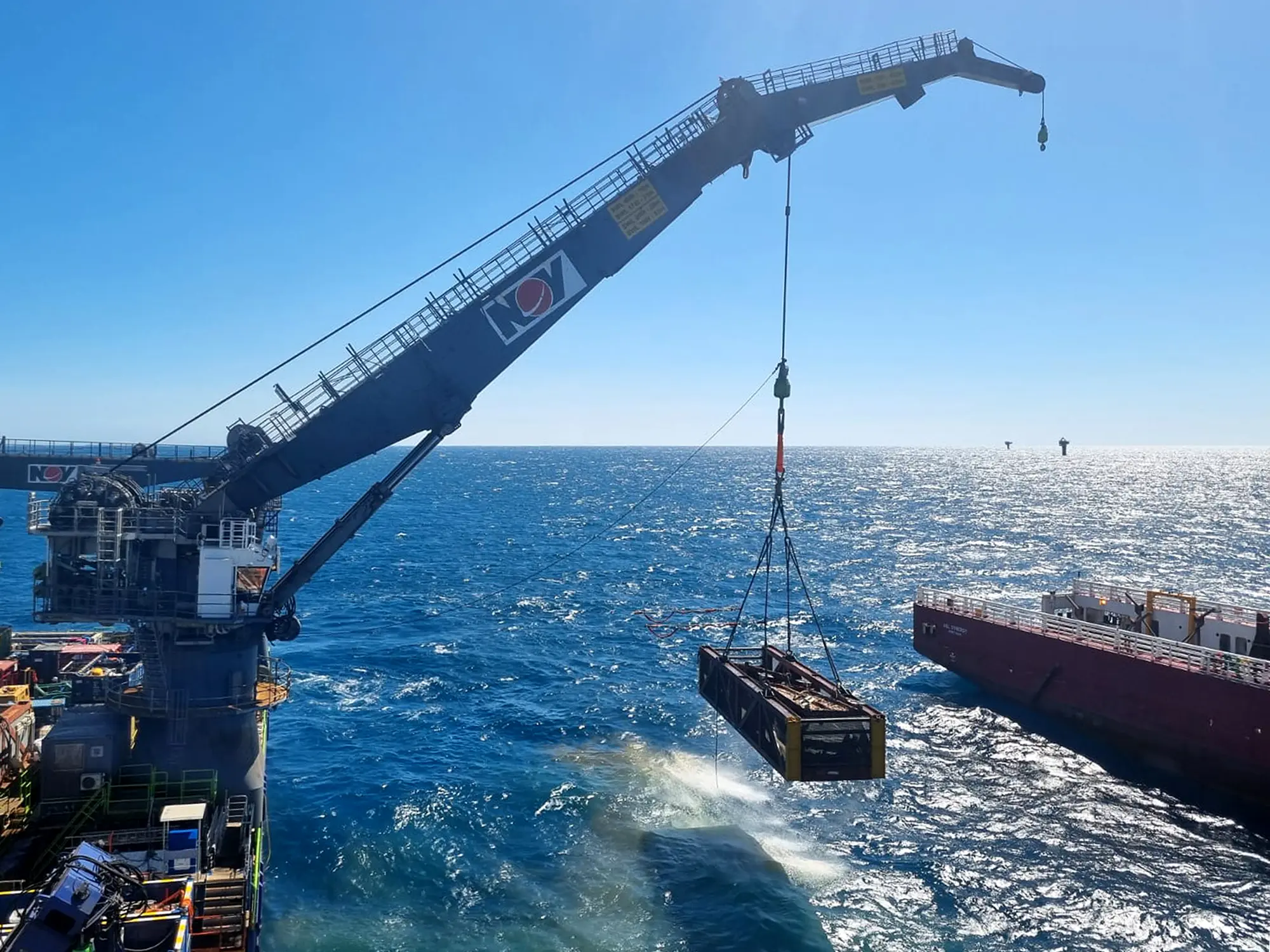 Large metal platform suspended by cables over ocean near offshore oil rig at sunset.