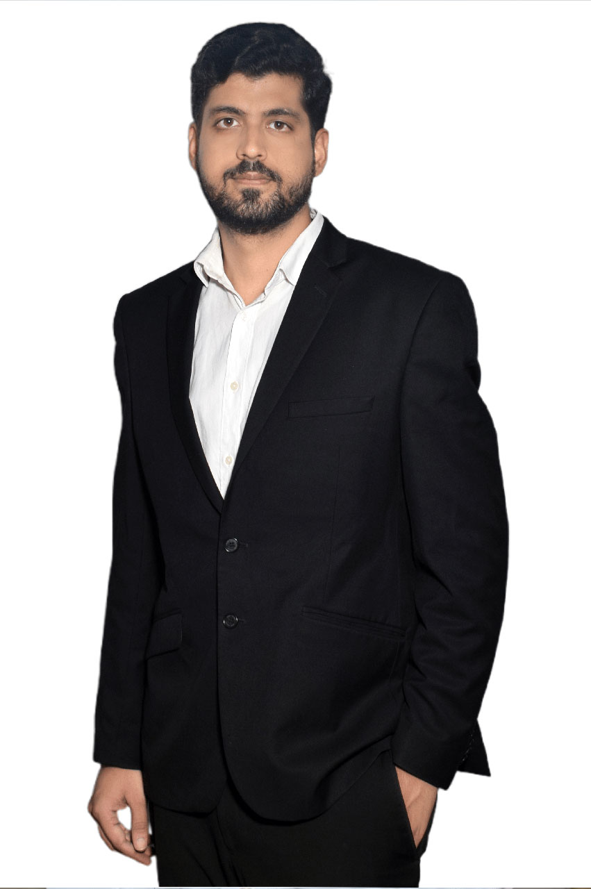 Man with a beard wearing a black suit jacket and white shirt standing against a white background.