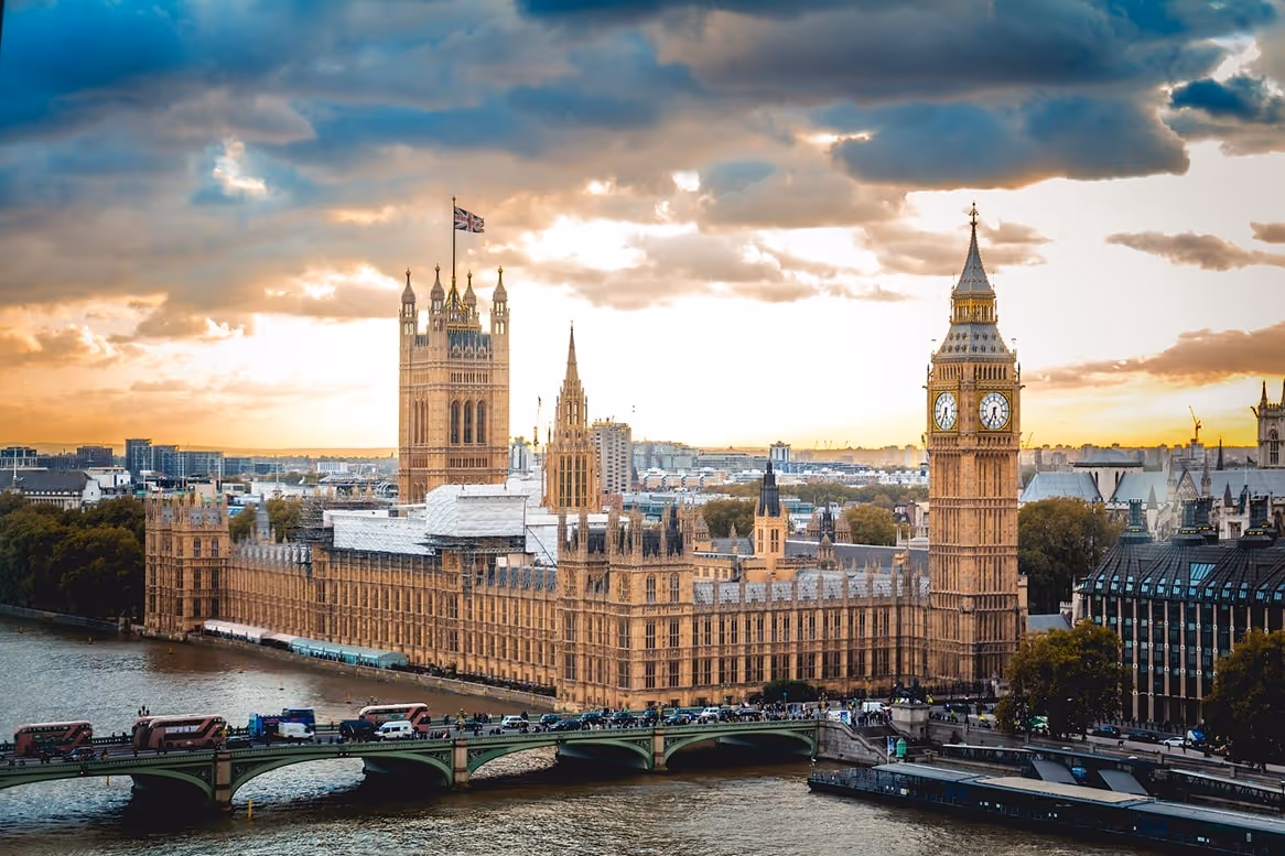 View of the Houses of Parliament and Big Ben in London with Westminster Bridge over the River Thames at sunset.