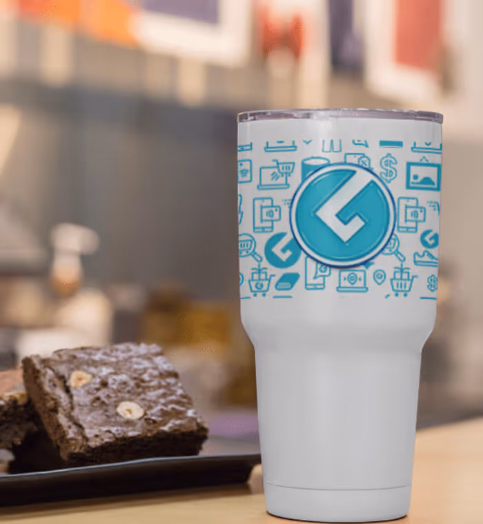 White insulated tumbler with a blue logo and icons, next to pieces of chocolate brownies on a black plate.