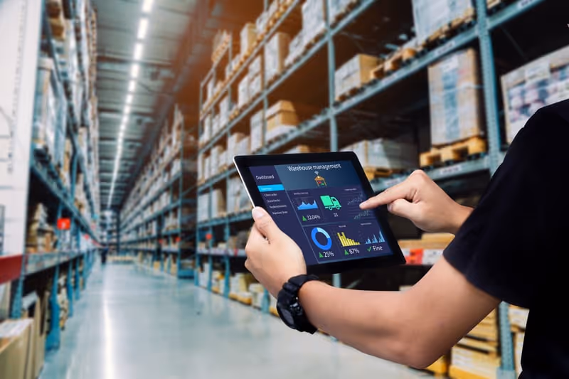 Person using a tablet displaying warehouse management dashboard in a large inventory warehouse.