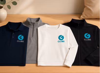 Four folded shirts in navy polo, gray quarter-zip, white crewneck, and black full-zip, each with a blue 'G Clubs' logo on the chest, displayed on a wooden surface.